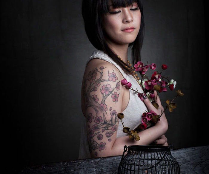 Japanse tatoeages voor vrouwen, vrouw met kort zwart haar en tatoeage van kersen in haar bovenarm
