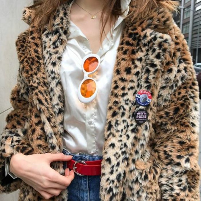 Mulher dos anos 80 com uma jaqueta leopardo, camisa de cetim branca, calça jeans vermelha, óculos de sol brancos com lentes laranjas