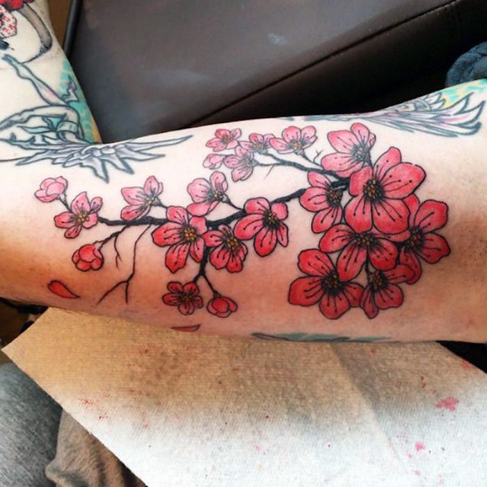 gekleurde bloemtattoo op de bovenarm, tak met rode bloemen