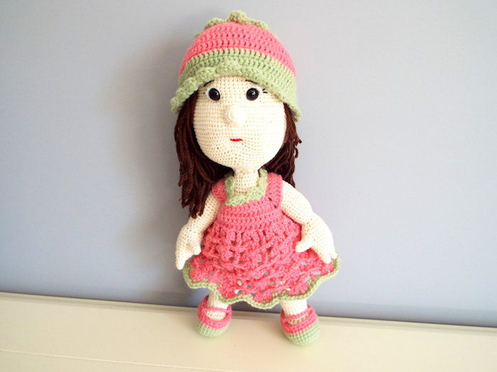 en dukke med rosa og grønn kjole, små svarte knapp øyne og brunt hår - hekle lykke charms