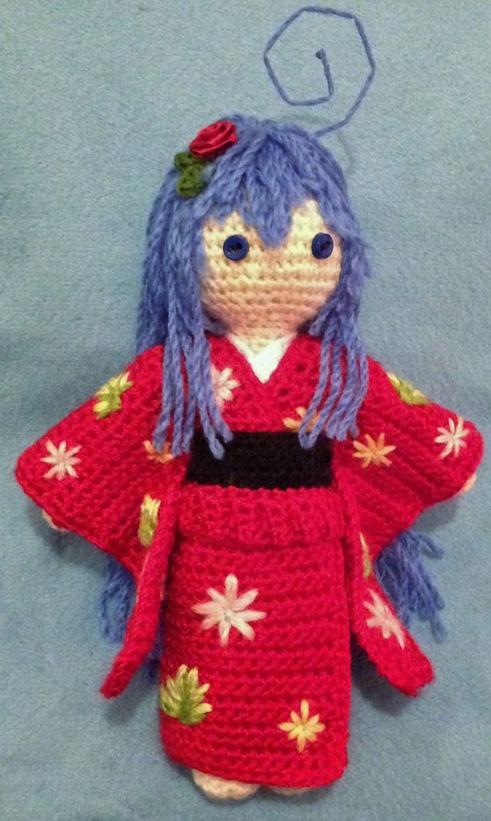 en japansk dukke laget av anime, lilla hår og rød kjole med en rose