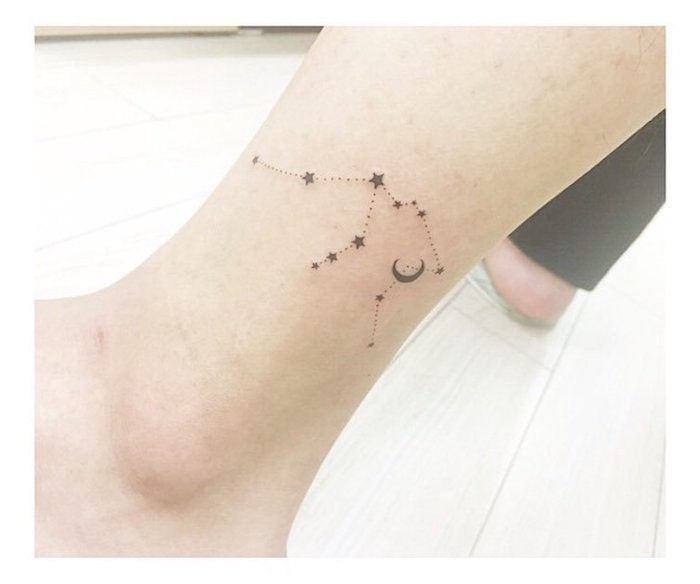 tatuaggio stella nera - una gamba con un piccolo tatuaggio nero con un'immagine stellare con piccole stelle nere e una luna nera