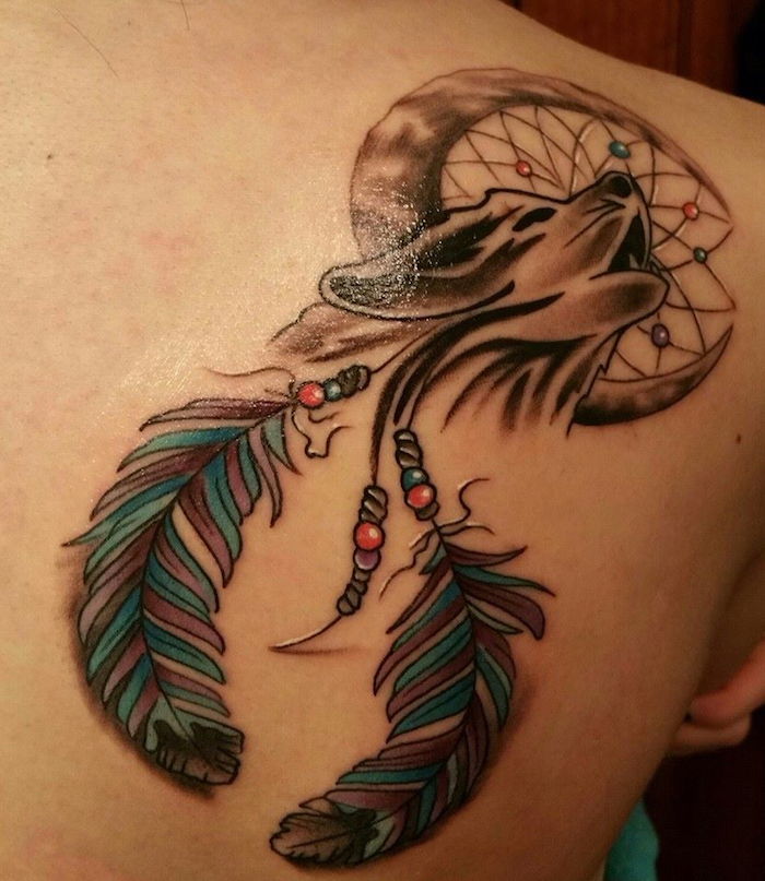 aceasta este o idee minunata pentru catcherul de vis de tatuaje cu un lup negru care urla cu o luna si doua pene albastre - tatuaj pe lama umerilor unei tinere