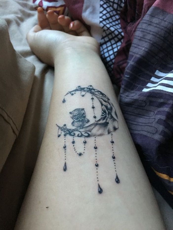 una luna nera e un piccolo gufo carino - idea per un tatuaggio sul polso di una giovane donna