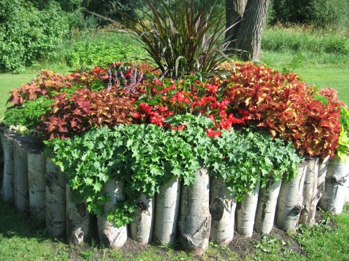 okrúhly kvetináč vyrobený zo stromových kmeňov plných červených kvetov - ľahká starostlivosť o záhradu