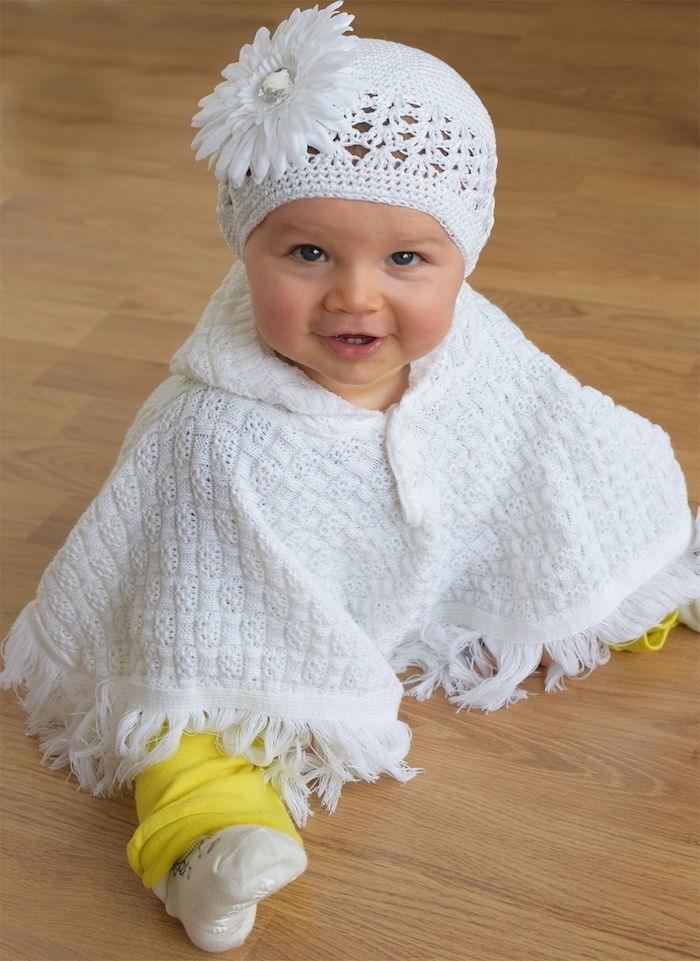 een schattig klein meisje met witte poncho als je voor baby poncho breit