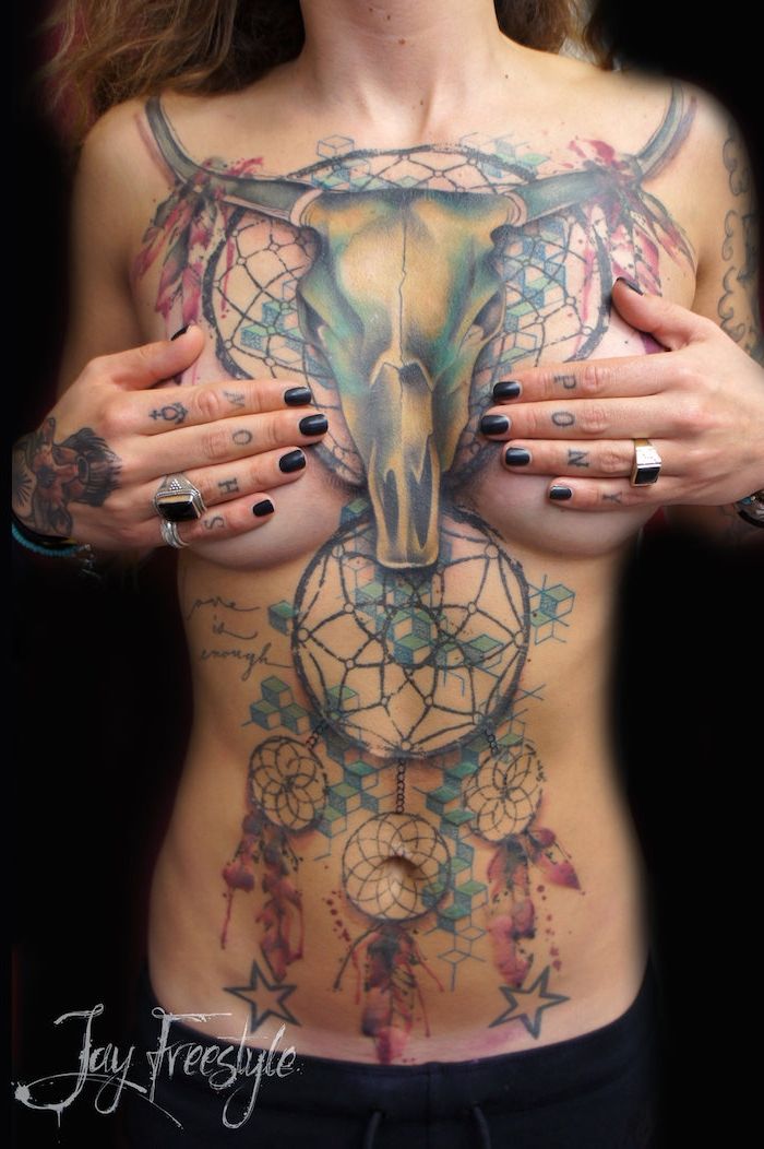 O femeie tânără cu multe tatuaje, cu capcane de vis, craniu, stele și pene violete