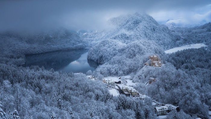 belle immagini invernali - una foresta con molti alberi con neve e lago e un piccolo castello giallo - cielo con molte nuvole grigie