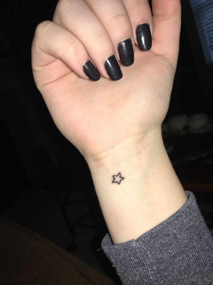 una mano con un piccolo tatuaggio nero con una piccola stella - mano con le unghie con uno smalto nero