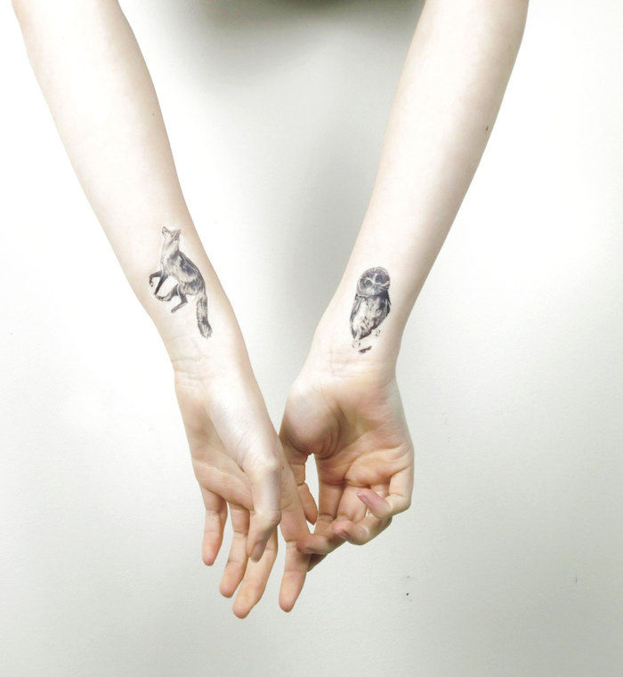 Qui ci sono due mani con piccoli tatuaggi sul polso - gufo e volpe