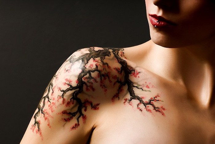 Vrouw met kersenbloesem tattoo op schouder, tak met rode bloemen