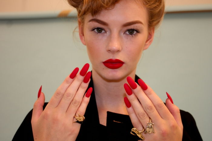 gel naglar spetsig kvinna modell med röda läppar och röda långa gel naglar gyllene ringar dekoration retro stil smink frisyr