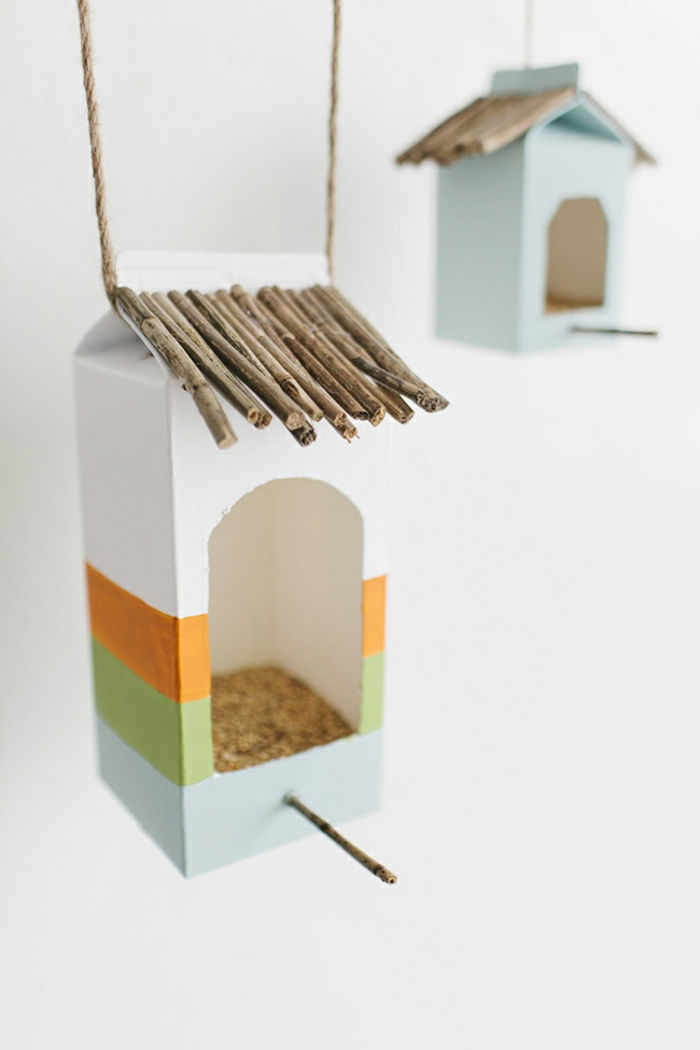 Casette per uccelli fatte di cartone di latte da soli, riempite di semi e semi di girasole, attaccatevi sui bastoncini