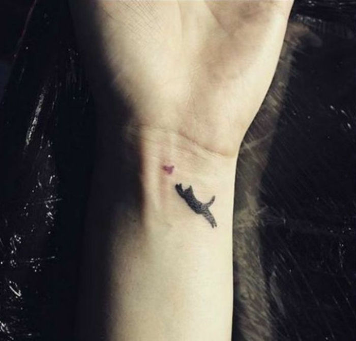 To jest ręka z małym tatuażem z czarnym kotem i ptakiem - pomysł na tatuaż na nadgarstku