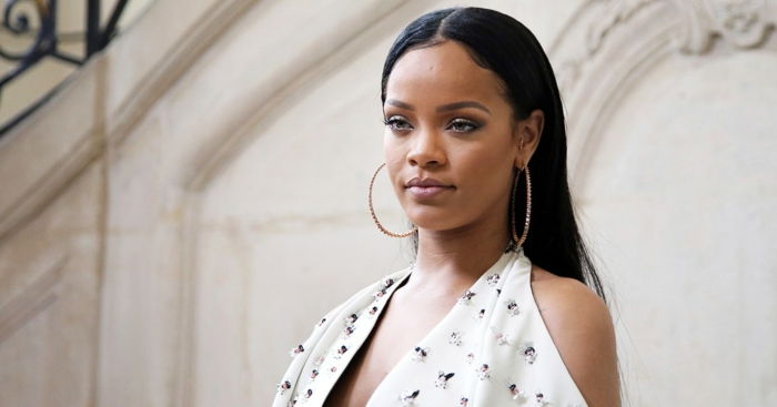 czarna gładka fryzura - włosy Rihanna, duże złote kolczyki, biała sukienka ze wzorem