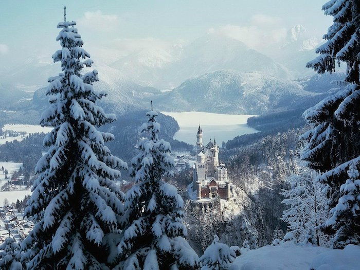 una romantica scena invernale con un castello bianco con torri e una foresta con molti alberi - montagne con neve - cielo blu con nuvole bianche
