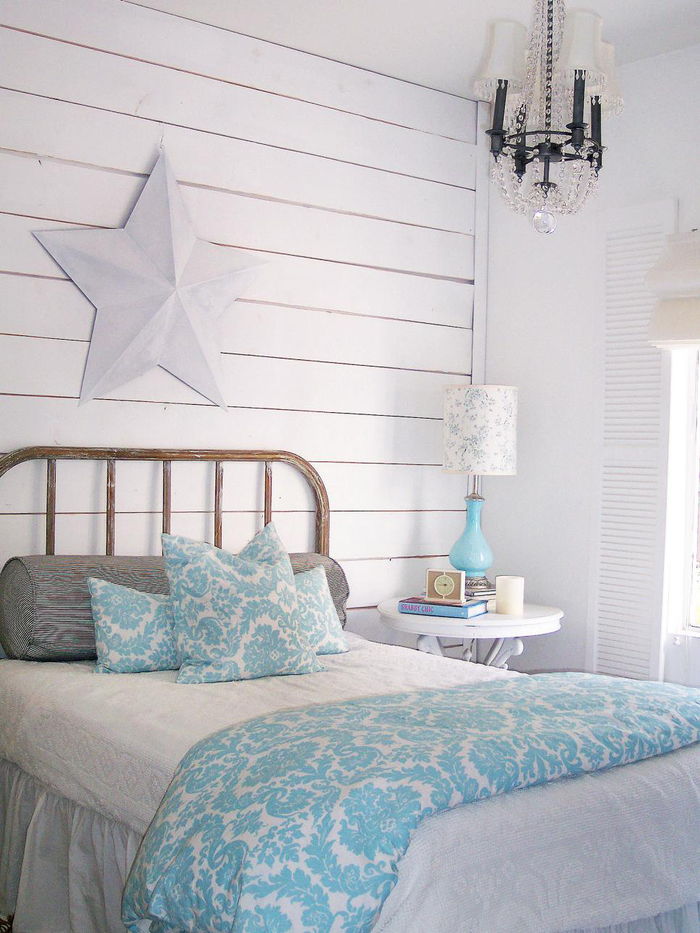 spalnica v beli barvi, svetlo modra odeja in nočna svetilka, zložen eleganten