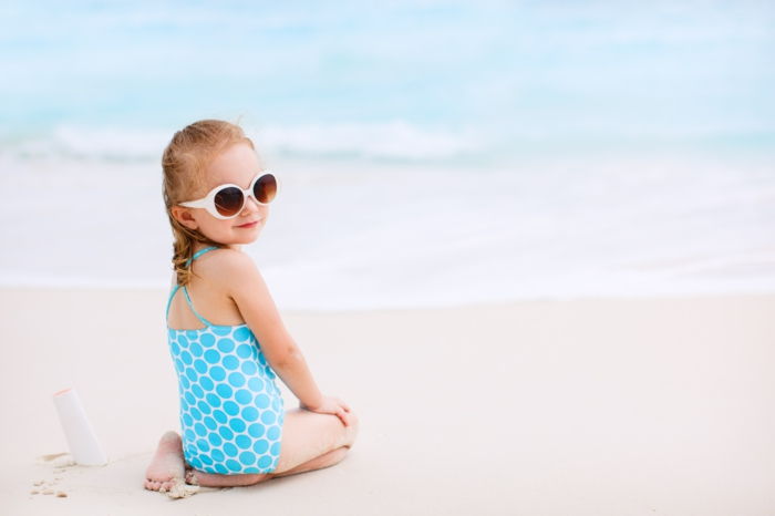 Liten jente med flaske solkrem på tropisk strand