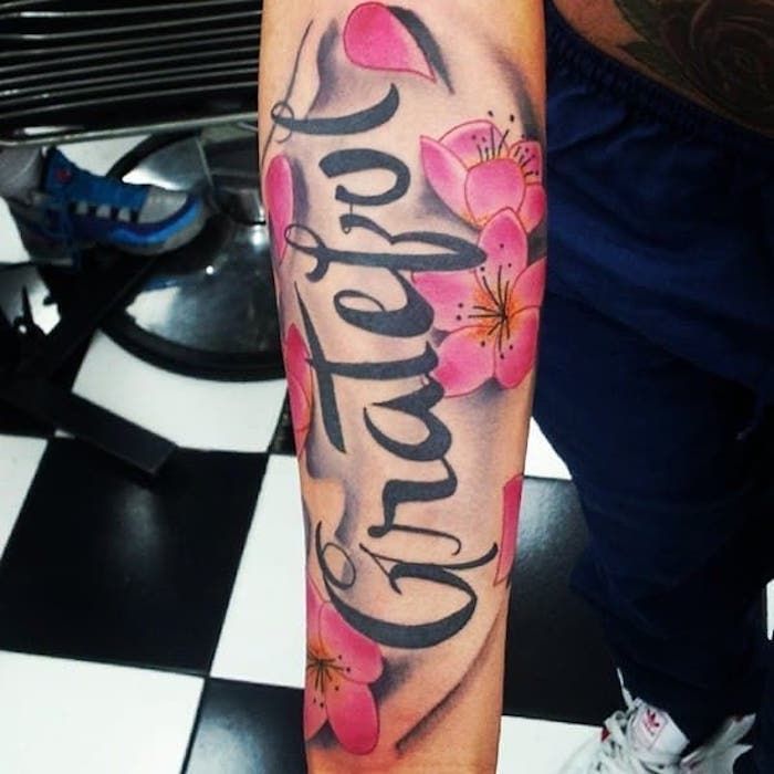 tattoo-belettering in combinatie met roze kersenbloesems, onderarmtattoo