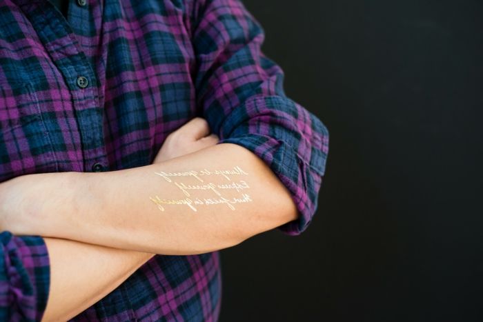 belas tatuagens palavras douradas em pé no braço e embelezar o corpo roxo camisa azul