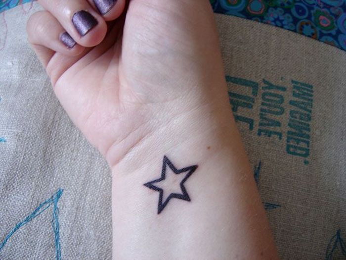 Mano con uno smalto per unghie viola e un piccolo tatuaggio con stella nera