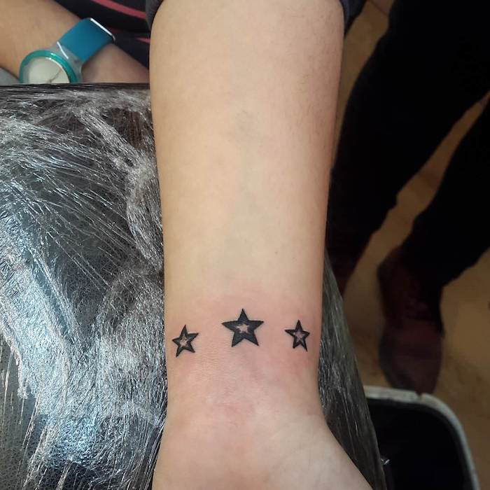 Una mano che regge una stella nera del tatuaggio con tre piccole stelle nere tatuate al polso