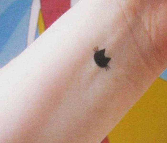 Oto mały czarny tatuaż na ręce - czarny kot z czarnymi długimi ogonami na swoim fiutku