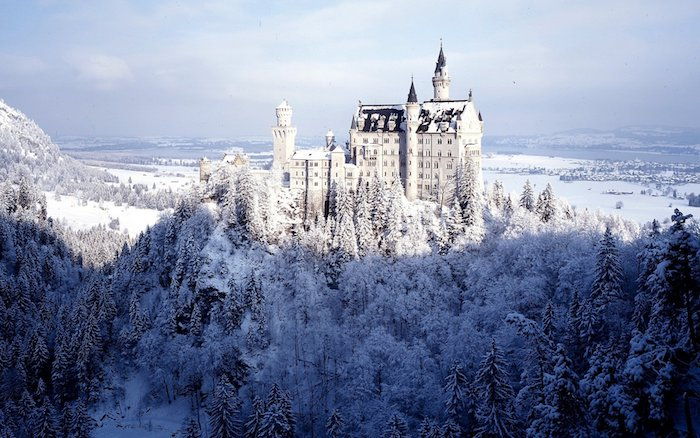 Immagine invernale con un grande castello bianco con torri e una foresta con molti alberi con la neve - un cielo con nuvole bianche