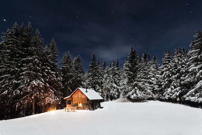 una piccola casa di legno e una foresta con molti alberi e neve - un cielo con stelle bianche e nuvole