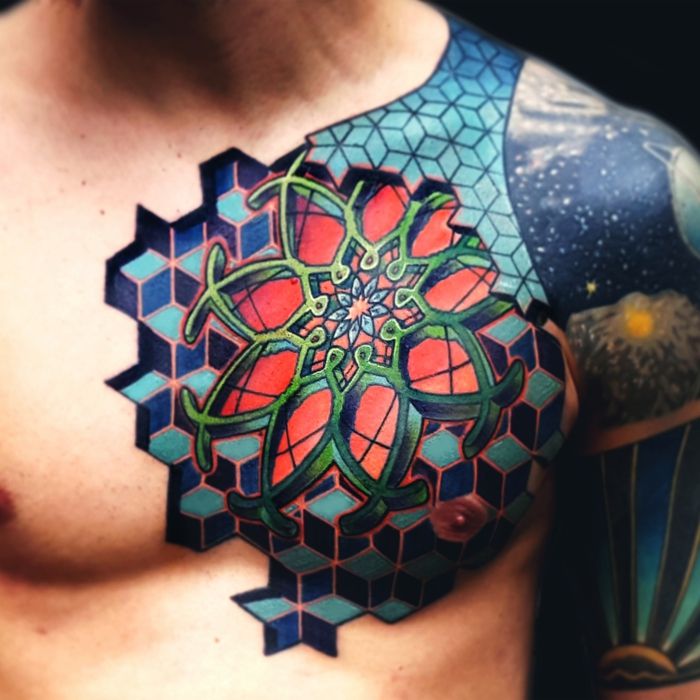 Mandala tatuering med 3-D effekt, ung man med färgad brösttatuering med geometriska motiv i blåa färger. Man med axeltatuering i blå toner