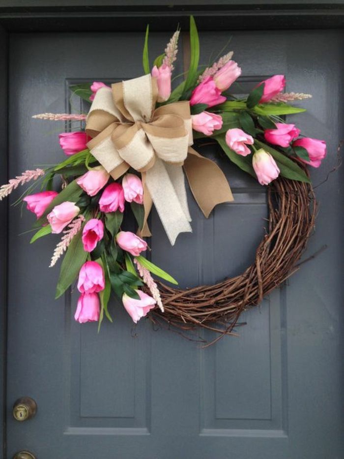 Decorazione di primavera armeggiare, porta grigia. decorazione della porta, ghirlanda di rami decorati con tulipani e fiocco beige di lino