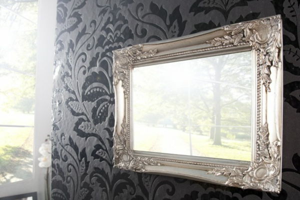 baroko veidrodis su sidabro rėmeliu ant sienos su juodu tapetu, įdomus