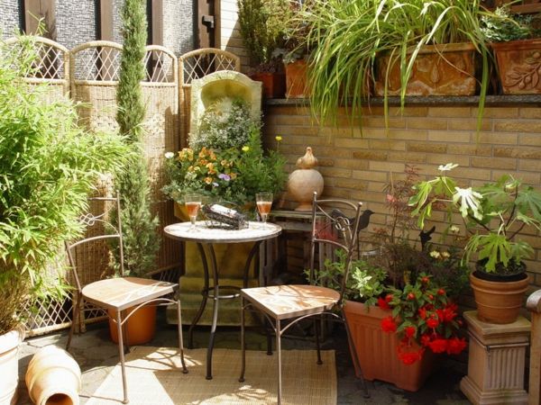 Terasa su žaliais augalais, apvalus stalas ir du kėdės