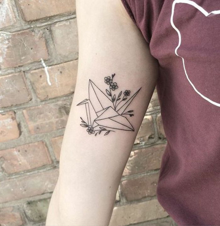 Oto dłoń z małym czarnym tatuażem origami - latający gołąb origami i małe kwiaty
