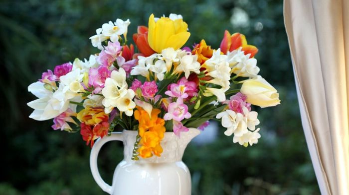 Jarná kytica v porcelánovej váze, farebné frézy a tulipány pri okne, prinášajúc jarnú náladu domov