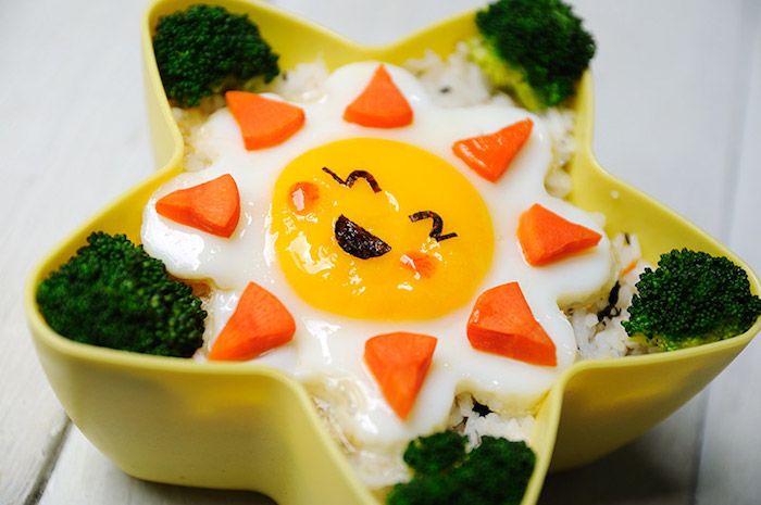 maža saulė pagaminta iš kiaušinių, ryžių su petražolėmis ir brokolių gėlėmis kaip šalutinė, geltona plastikinė dėžutė žvaigždės forma