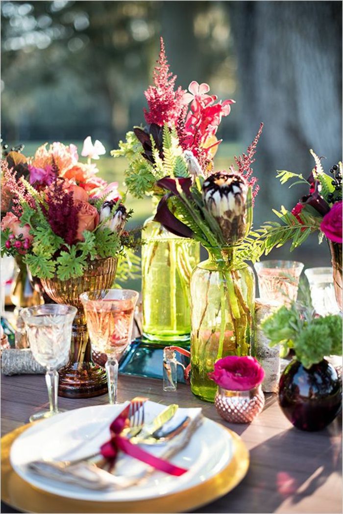 şenlikli masa dekorasyonu, kristal bardak, pembe fiyonk, birçok çiçek, cam vazolar