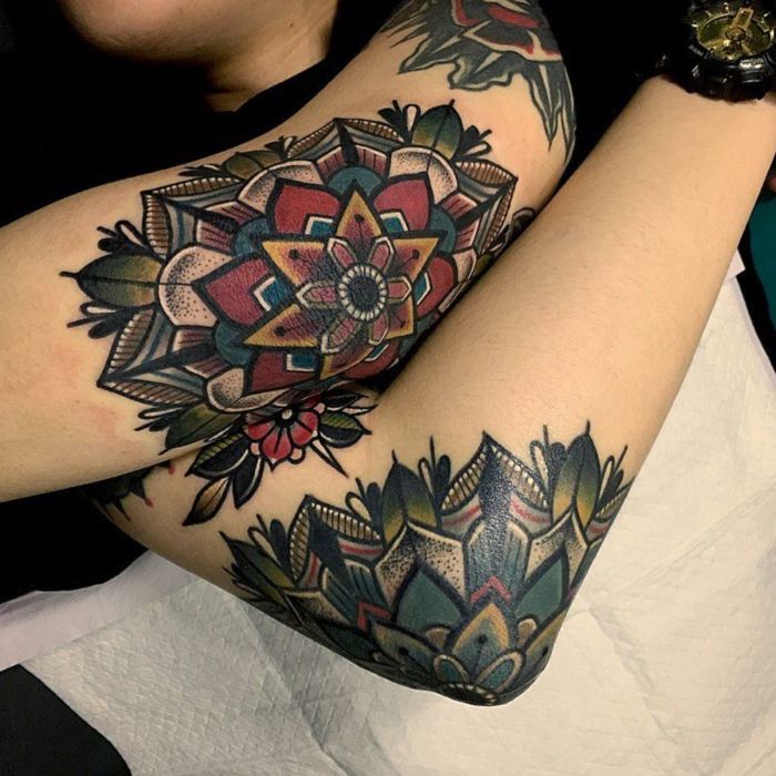 Kvinna i en tatueringstudio med tre färgade tatueringar - en axel, en övre arm och en armbåge tatuering, hon har en svart klocka med en guldpläterad urtavla