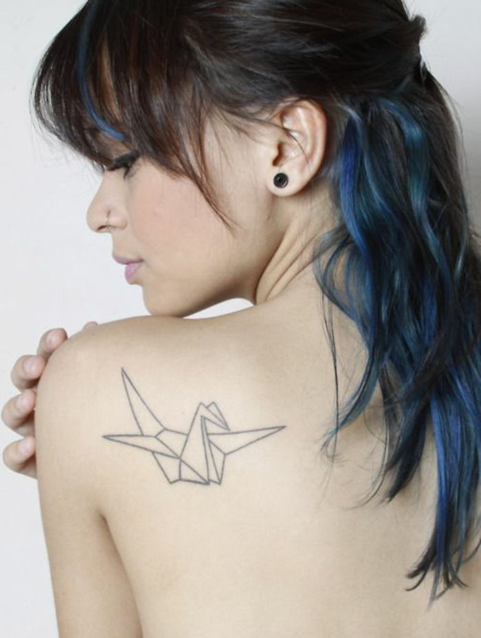Oto młoda kobieta o niebieskich włosach i małym tatuażu origami na łopatce - białym latającym origami dove