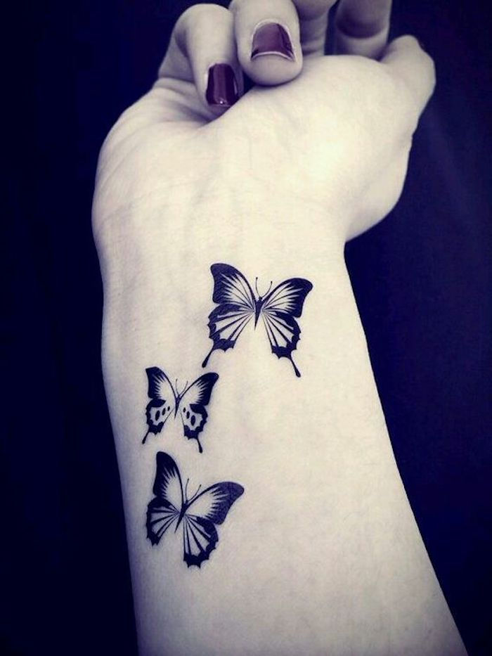 tai yra viena iš geriausių tauriųjų tatuiruočių idėjų, kurią galite tikrai patikti - trys mažos, juodos, plaukiojančios drugelės ant riešo jaunos moters ranka