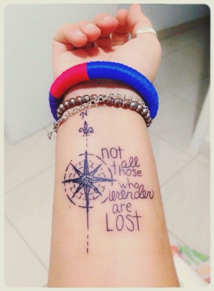 Moterio ranka su žiedu ir juoda tatuiruotė su kompasu su juodomis antraštėmis