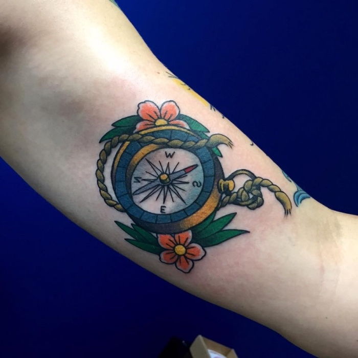 Her er en ide for en tatovering med et lite kompass med to røde blomster og små grønne blader - en fabelaktig tatovering på hånden