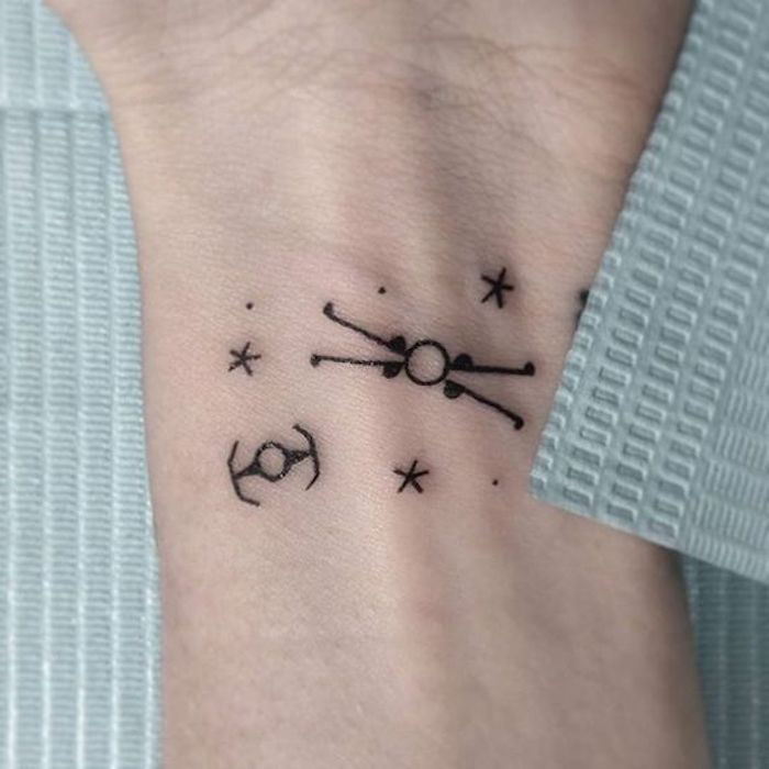 nápad na tetovanie hviezdnych vojen na zápästí - čierne malé tetovanie s malými čiernymi hviezdami a planétami a malými lietajúcimi vesmírnymi loďami hviezdnych vojen