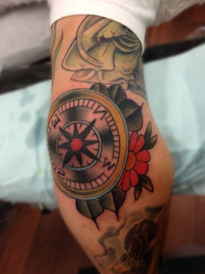 en kompass med en röd blomma och gröna blottar - idé för en saga kompass tatuering på en hand