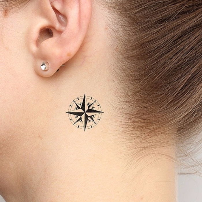 kompaso tatuiruotė - jauna moteris su tatuiruotėmis su juodu mini kompasu ir mažais auskarais