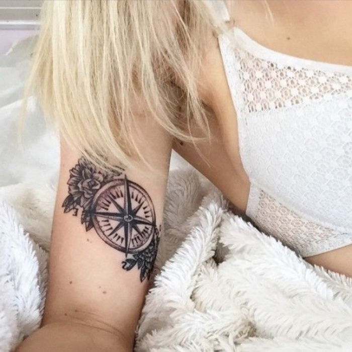 Her finner du en av våre ideer for en liten svart tatovering med svart kompass og små svarte blomster - en ung kvinne med kompasstatovering på hånden hennes