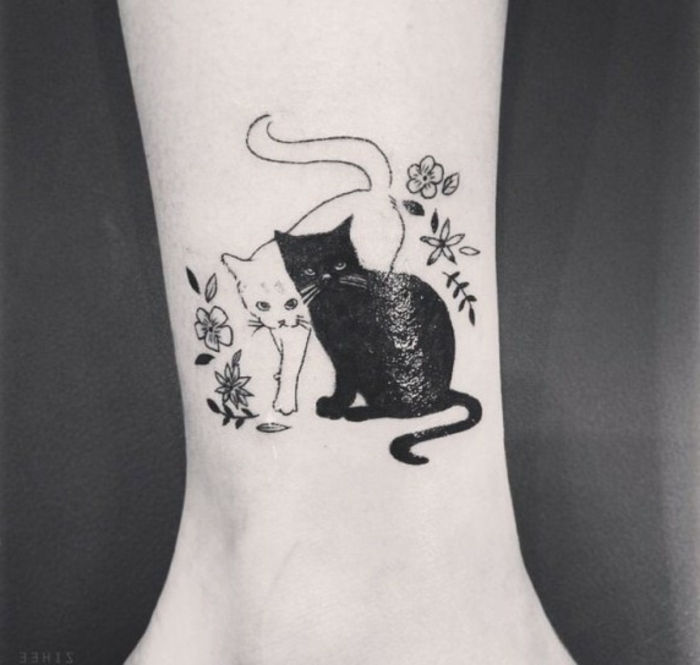mały czarny i mały biały kot z kwiatami - pomysł na tatuaż kota na nadgarstku
