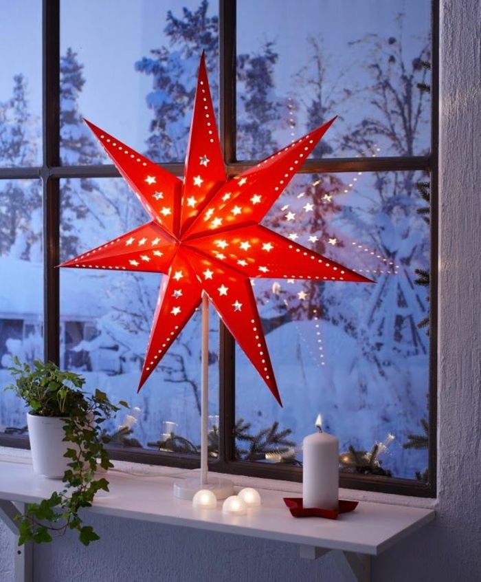 Gulvlampe med rød paraply i form av en stjerne, opplyst stearinlys av hvit voks, grønn surr i en hvit keramisk blomsterpotte, vinterlandskap med mye snø