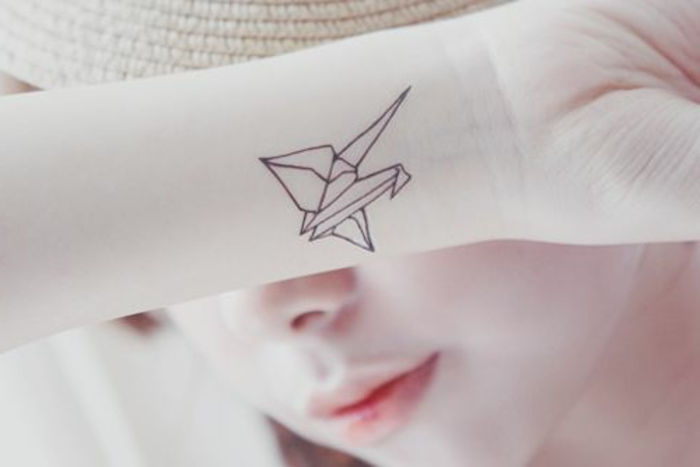 Oto młoda kobieta z małym tatuażem origami na nadgarstku - mały latający ptak origami na dłoni