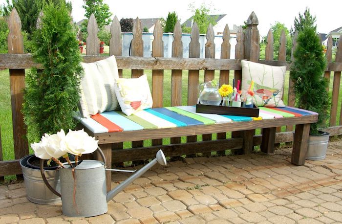 foto di giardinaggio - una panca da giardino in legno con tre cuscini bianchi - giardino e fiori bianchi e cancello del giardino